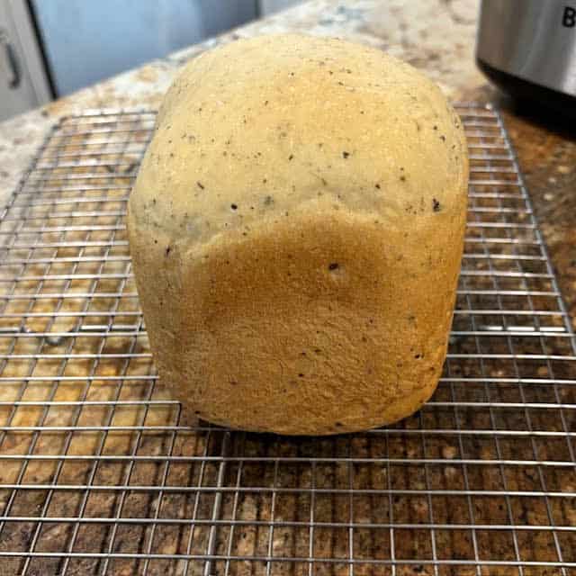 A loaf of bread machine Italian herb bread on a wore cooling rack.