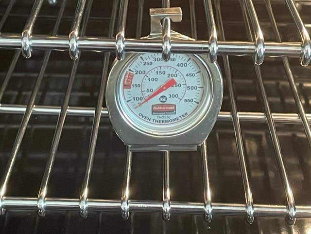 Portable oven thermometer sitting on wire grates in an oven.