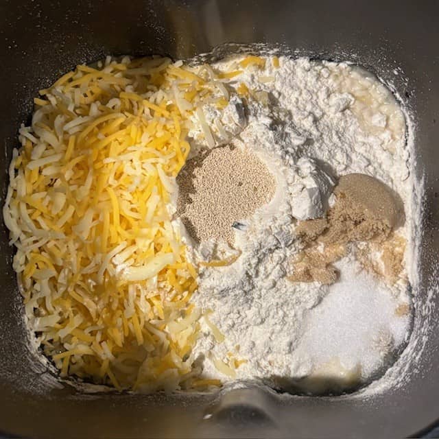 Ingredients for bread machine cheese bread in the bread machine's bread pan.