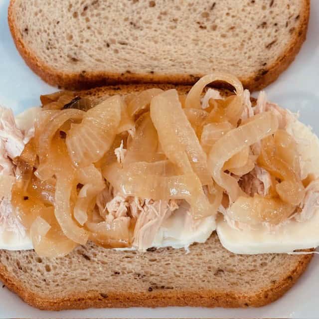 Sauteed onions on top of shredded chicken and mozzarella cheese on a slice of bread.