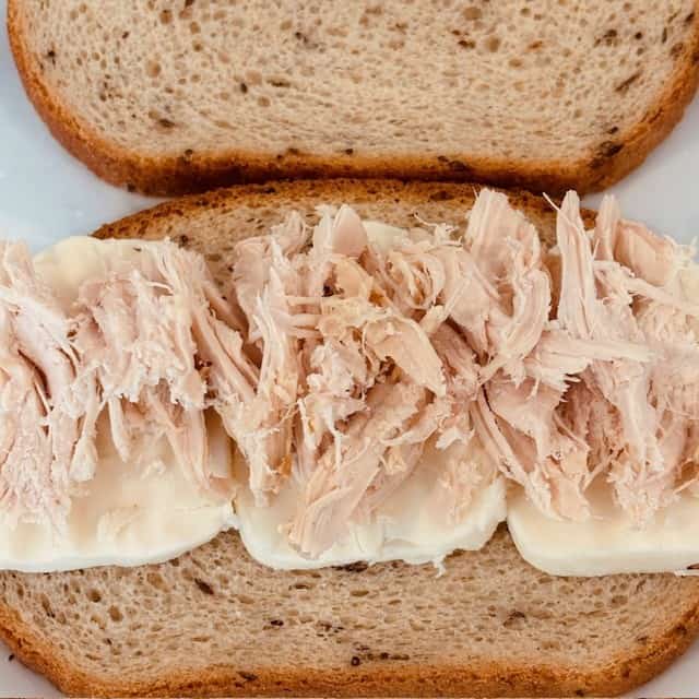Shredded chicken on top of mozzarella cheese on a slice of bread. 