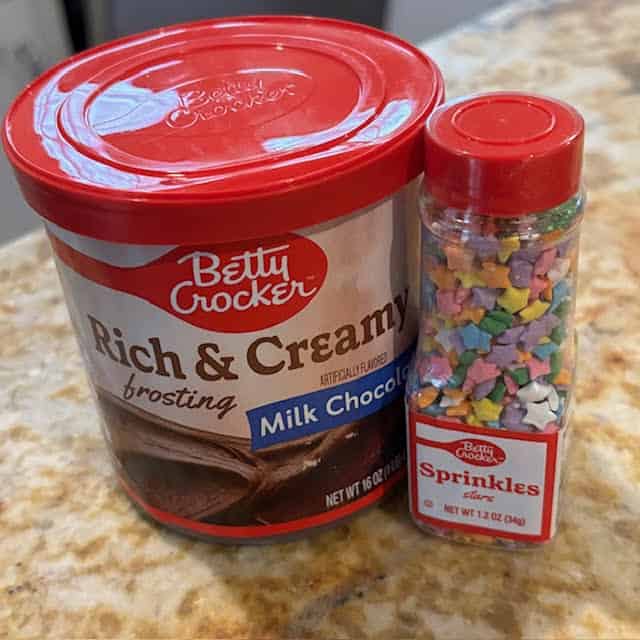 Containers of frosting and sprinkles on kitchen counter.