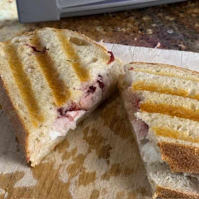 Turkey panini cut in half on a wooden cutting board.