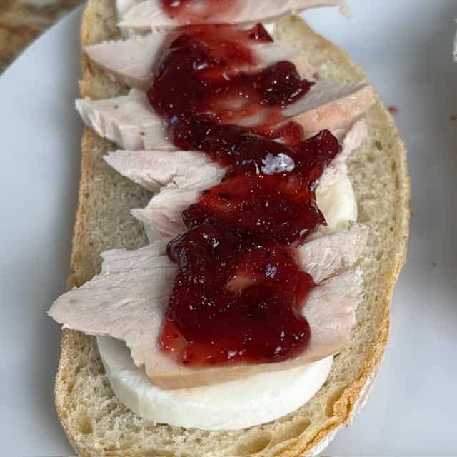 Turkey panini being assembled with turkey, mozzarella and cranberry sauce.