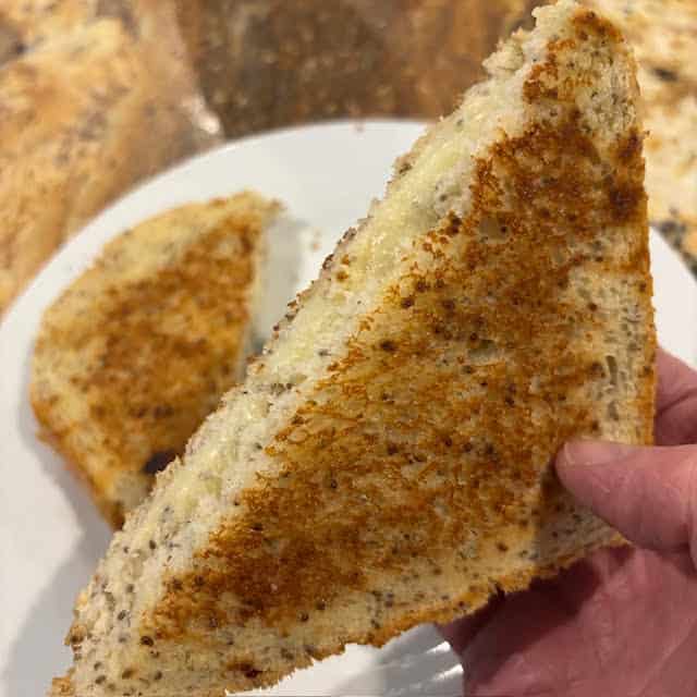 Hand holding a grilled cheese sandwich made with chai seed bread.