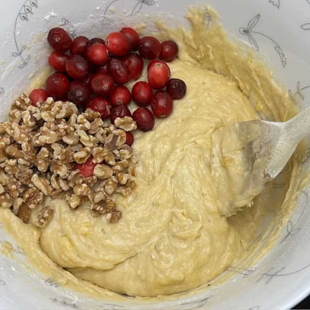 Cranberries and chopped walnuts being mixed into banana bread batter.