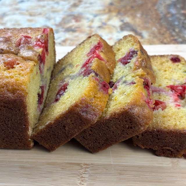 Slices of a moist cranberry orange bread on  a wooden cutting board.