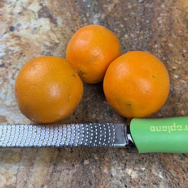 3 oranges and a zesting tool on a kitchen counter.