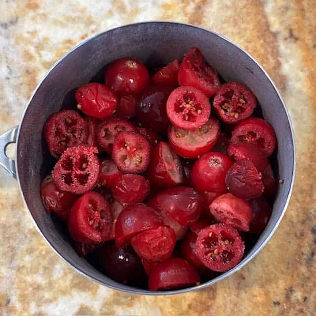 Cup of halved cranberries on kitchen counter.