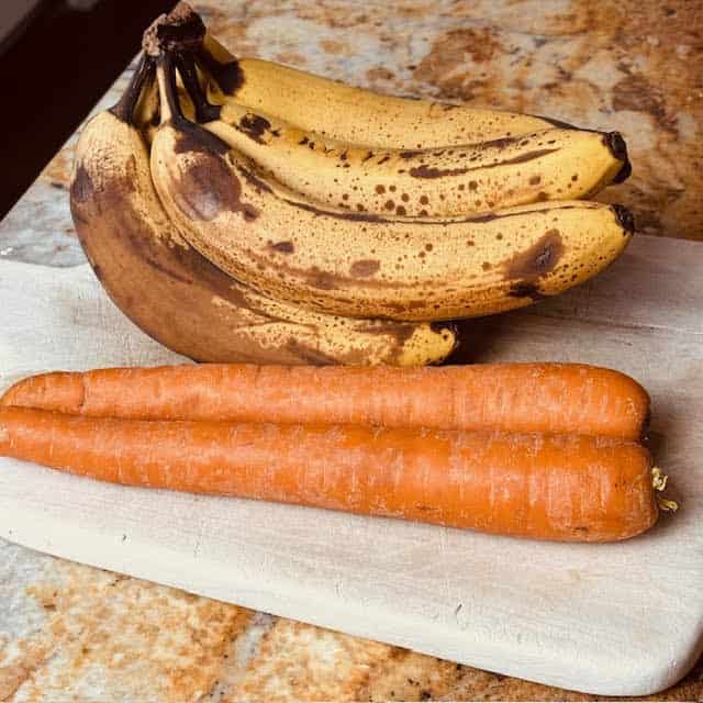 Bananas and carrots for carrot banana bread on a wooden cutting board.