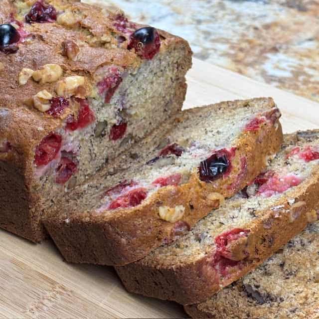 Slices of cranberry banana nut bread on a wooden cutting board.