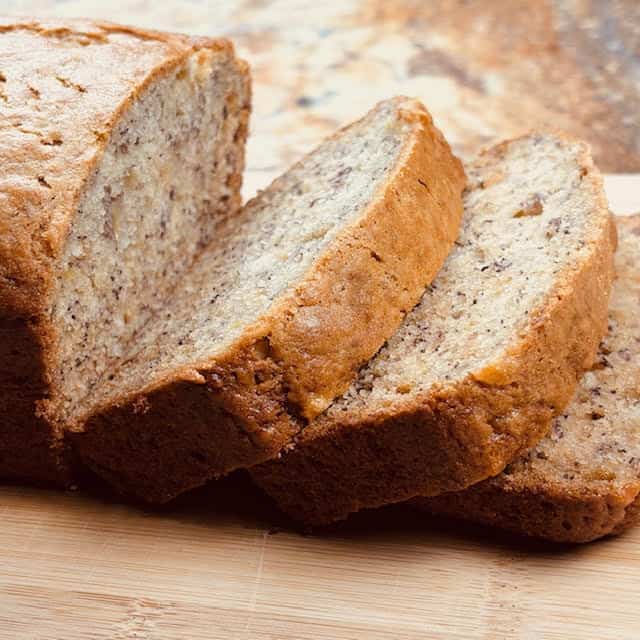 Slices of super moist banana bread on a wooden cutting board.