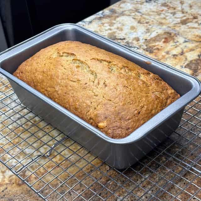 Super moist banana bread in pan on wire cooling rack.