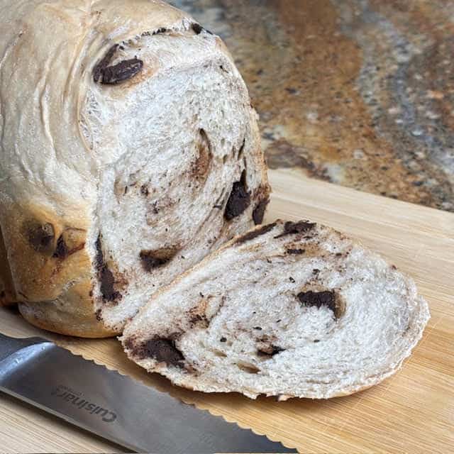 Sliced 1 lb bread machine chocolate chip bread and serrated knife on a wooden cutting board.