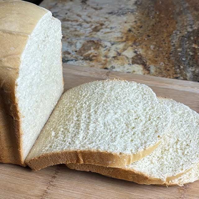 Slices of bread machine white bread on a wooden cutting board.