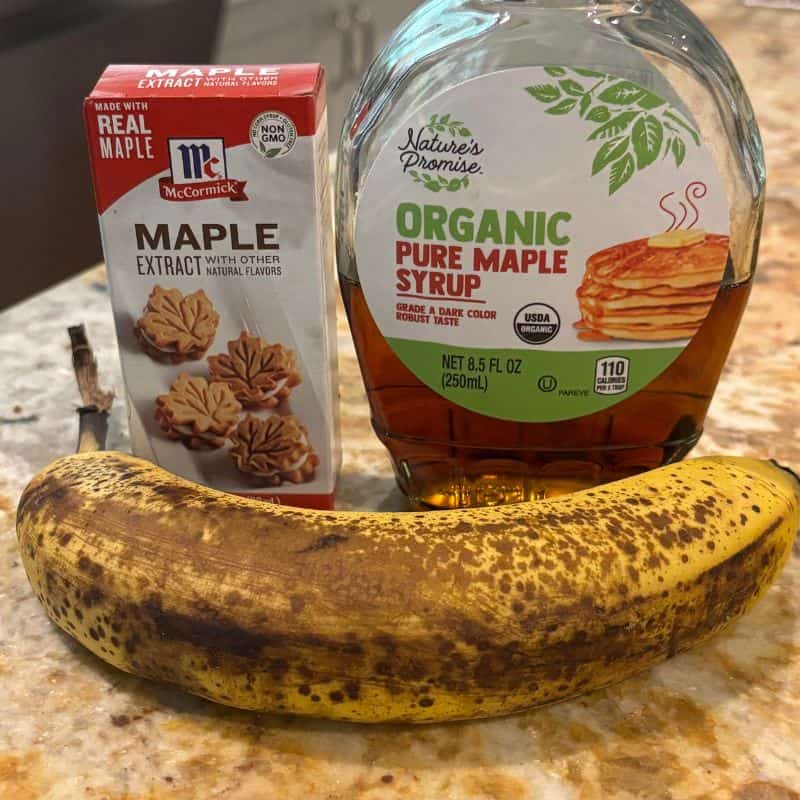 Maple extract, a bottle of maple syrup and a ripe banana on a kitchen counter.