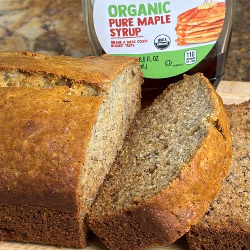 Maple banana bread with bottle of maple syrup on a wooden cutting board.