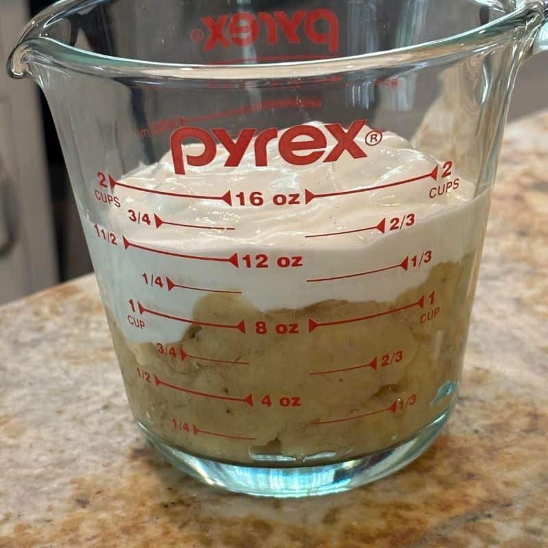 A measuring cup with Greek yogurt and mashed bananas in it in order to make a 2 banana nut bread.