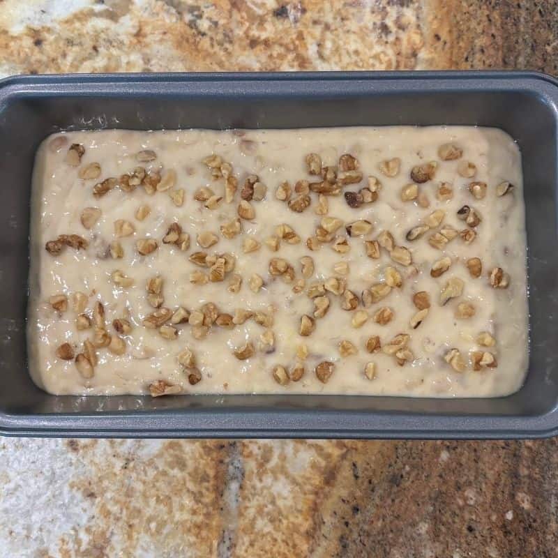 A bread pan containing the batter for 2 banana nut bread with a sprinkling of chopped walnuts on top of the batter.